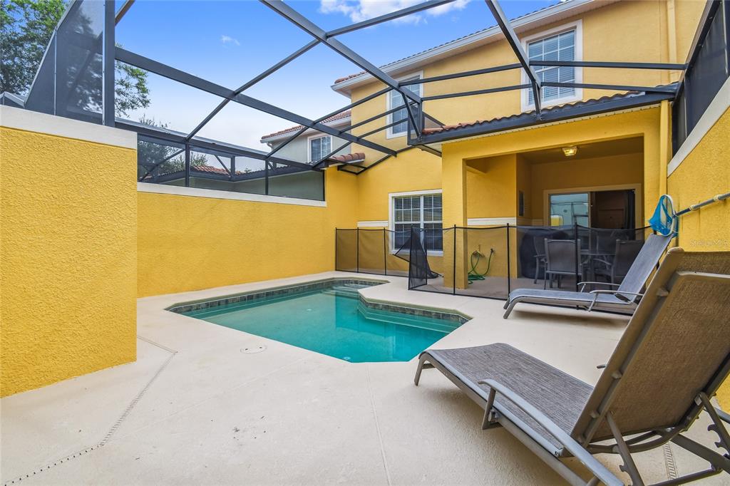 A screened-in patio features a swimming pool, lounge chairs, and a yellow stucco exterior wall — 8841 CANDY PALM ROAD, KISSIMMEE, FL