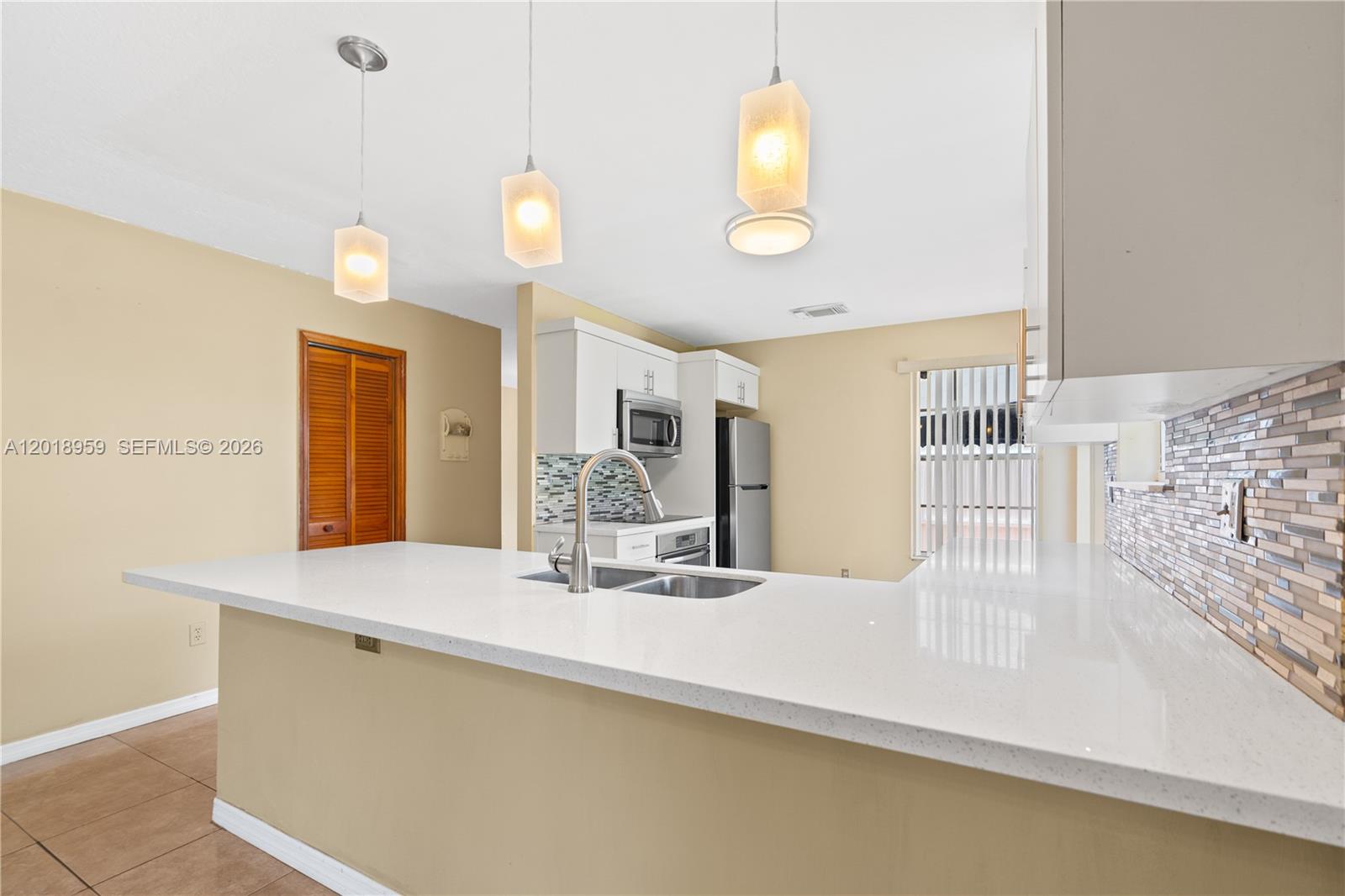 A kitchen features a white quartz peninsula countertop, stainless steel sink, and pendant lighting — 15345 SW 63rd Ter, Miami FL 33193, MIAMI, FL