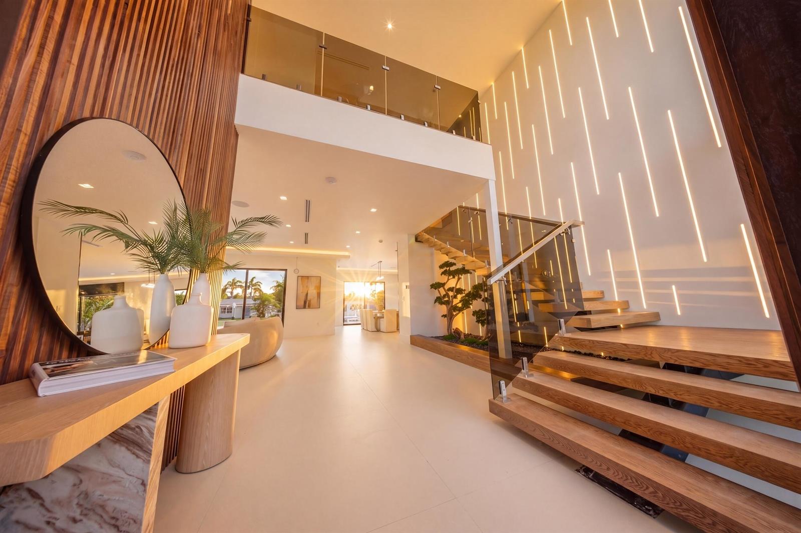 A modern foyer features a floating wooden staircase, vertical wall lighting, and a circular mirror — 2360 NE 49th Street, Lighthouse Point FL 33064, LIGHTHOUSE POINT, FL