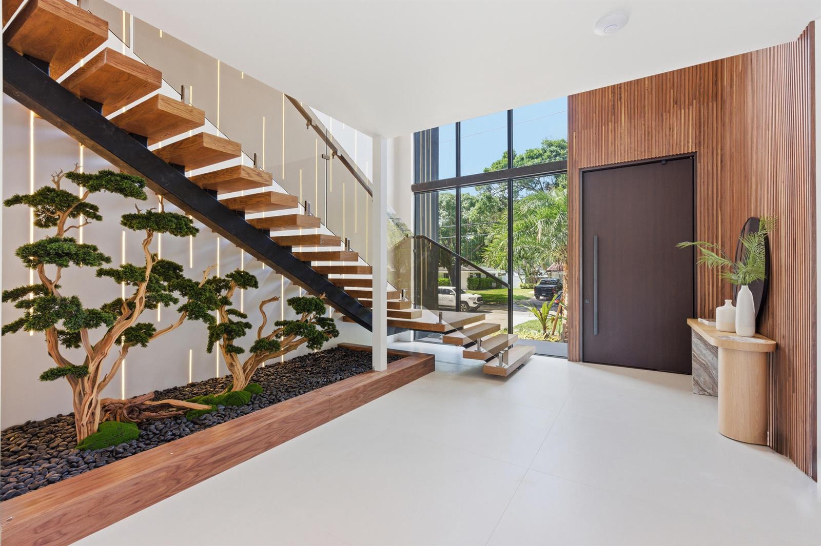 A modern entryway features a floating wooden staircase, a bonsai garden, and a large glass window — 2360 NE 49th Street, Lighthouse Point FL 33064, LIGHTHOUSE POINT, FL