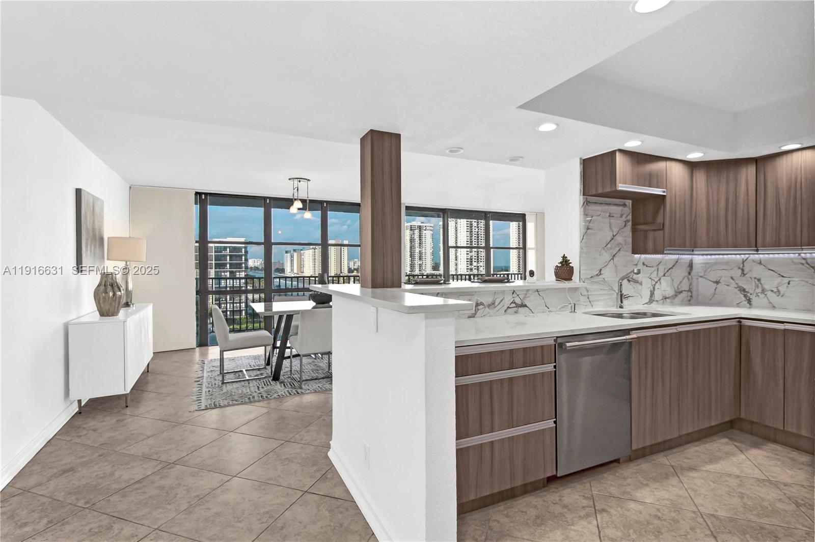 A modern kitchen with wood-toned cabinets and marble backsplash overlooks a dining area with views — 800 Parkview Dr # 821, Hallandale Beach FL 33009, HALLANDALE BEACH, FL