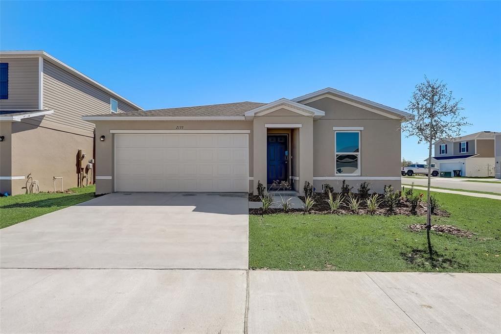 A single-story house with a two-car garage, blue front door, and tan exterior siding — 6903 LAKELAND BOULEVARD, FORT PIERCE, FL