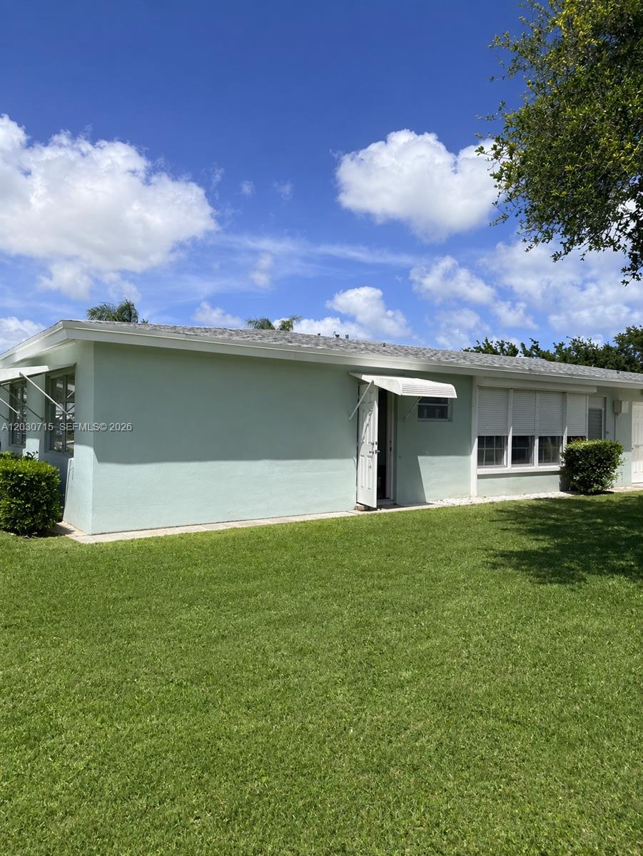 A light green single-story house features a white door, window awnings, and a grassy yard — 200 E High Point Ct E # D, Delray Beach FL 33445, DELRAY BEACH, FL
