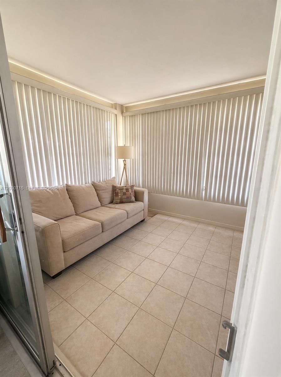 A sunroom features a beige sofa, tile flooring, and floor-to-ceiling vertical blinds — 200 E High Point Ct E # D, Delray Beach FL 33445, DELRAY BEACH, FL