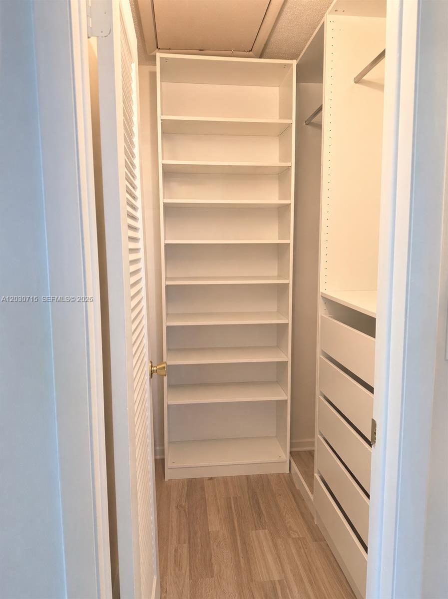 A walk-in closet features white shelving units and light wood-look flooring — 200 E High Point Ct E # D, Delray Beach FL 33445, DELRAY BEACH, FL