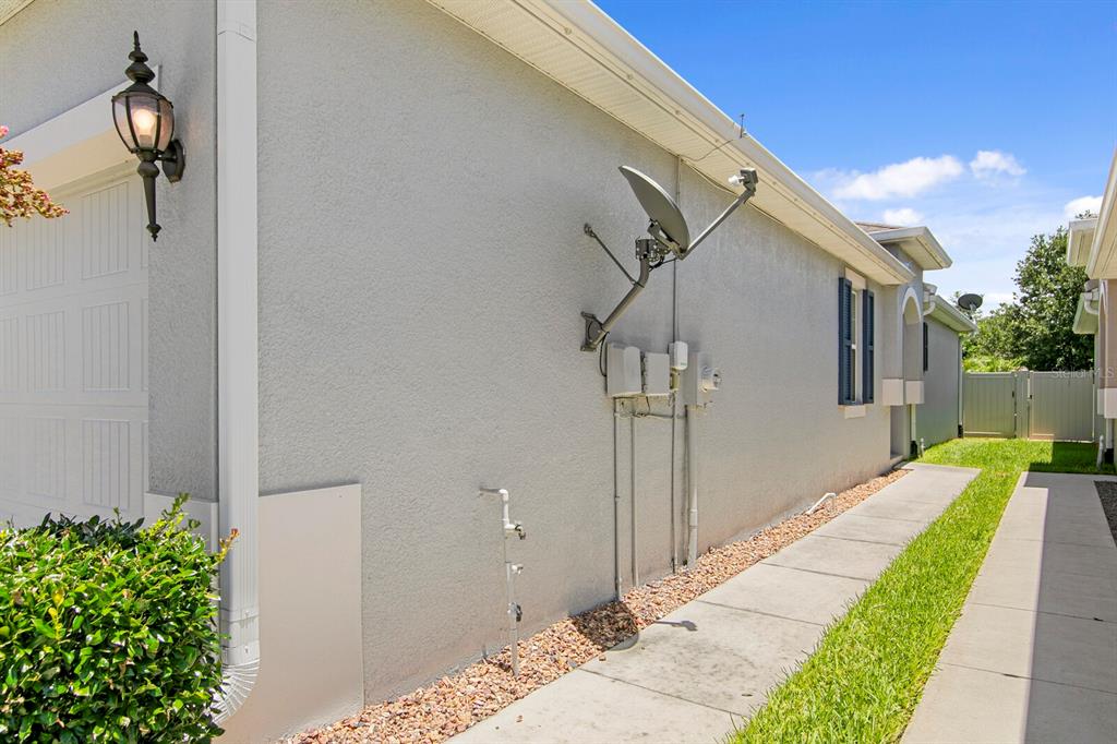 The exterior side wall of a house features a satellite dish, utility boxes, and a walkway — 10631 HERON HIDEAWAY LOOP, LAND O LAKES, FL