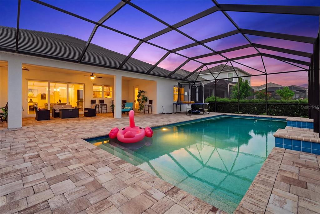 A screened-in patio features a swimming pool with a pink flamingo float and paver decking — 2641 BUTTERFLY JASMINE TRAIL, SARASOTA, FL