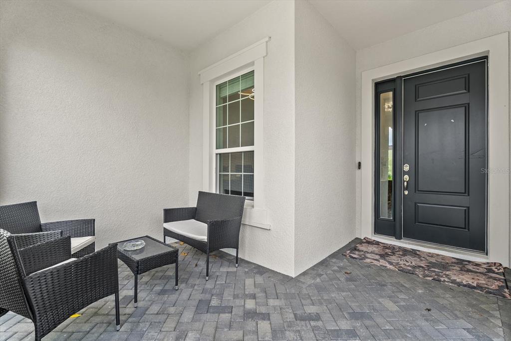 A covered front porch features gray brick pavers, black wicker furniture, and a dark front door — 2641 BUTTERFLY JASMINE TRAIL, SARASOTA, FL