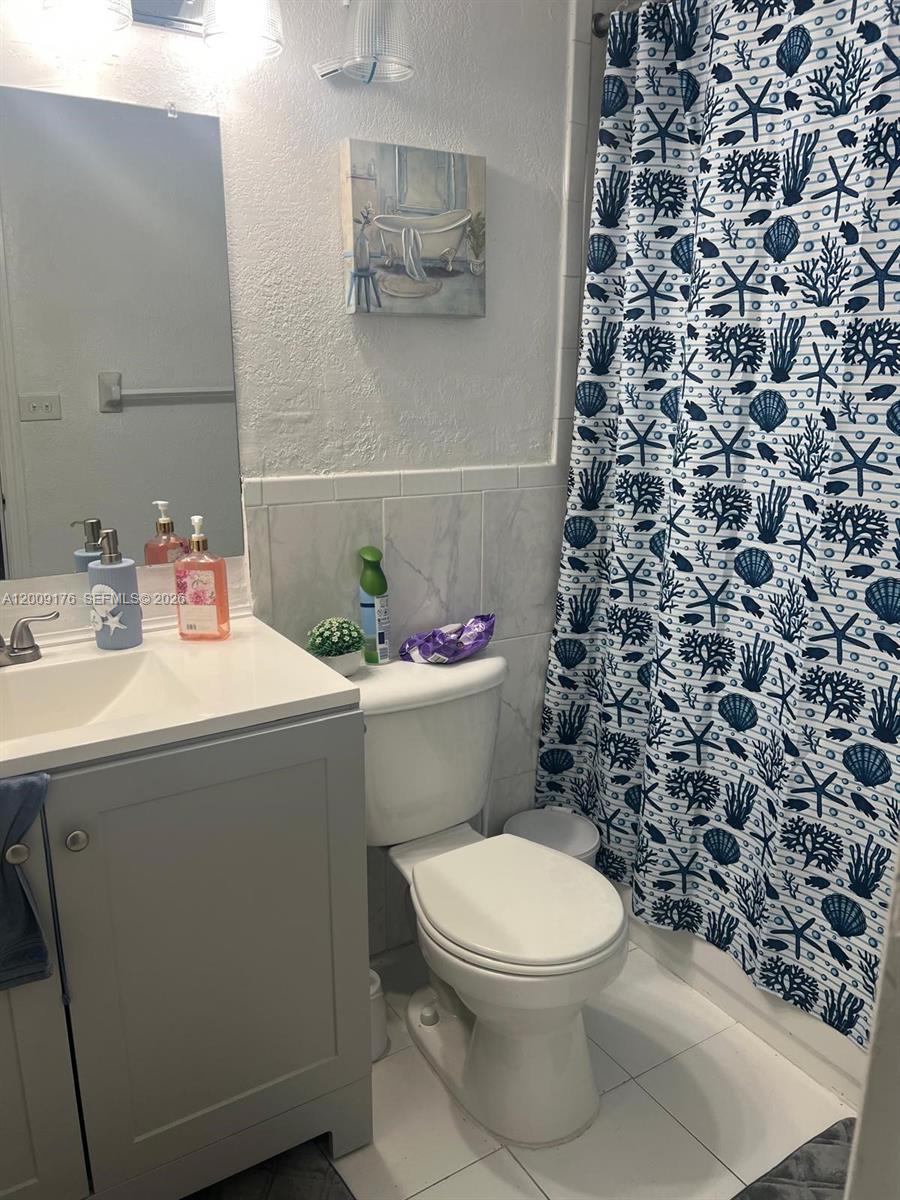 A bathroom features a gray vanity, a white toilet, and a blue-and-white patterned shower curtain — 801 NW 47th Ave # 503W, Miami FL 33126, MIAMI, FL