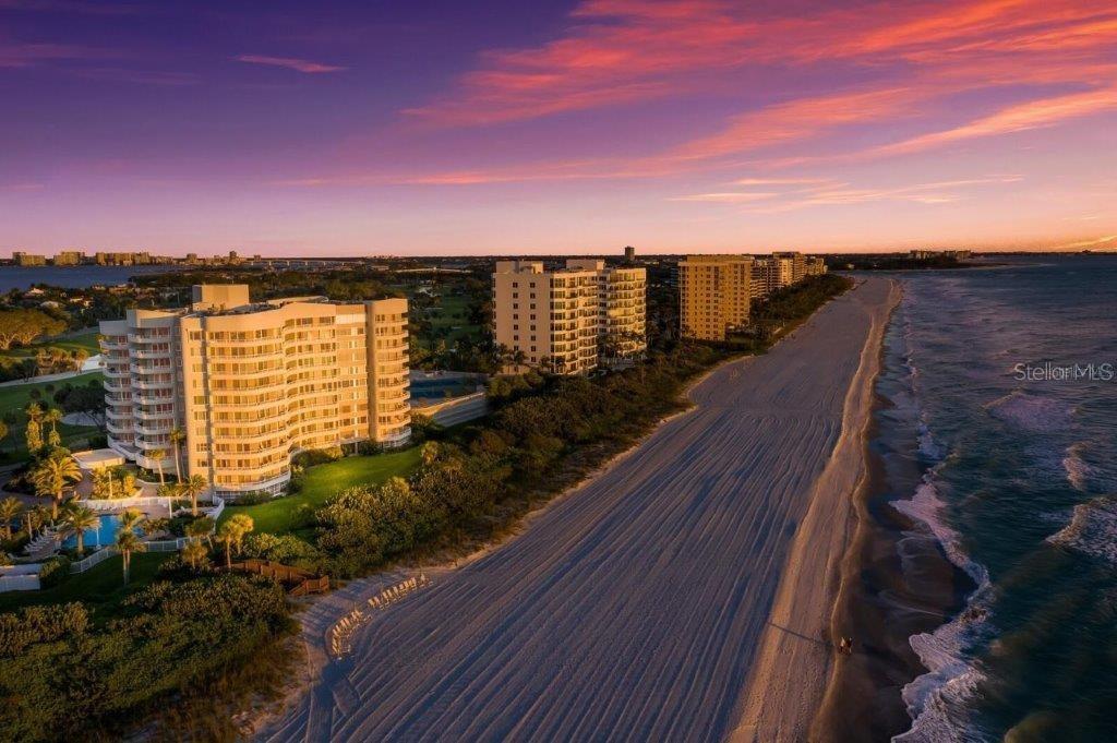 An aerial view shows beachfront high-rise condominiums along a sandy coastline at sunset — 775 LONGBOAT CLUB ROAD UNIT 808, LONGBOAT KEY, FL