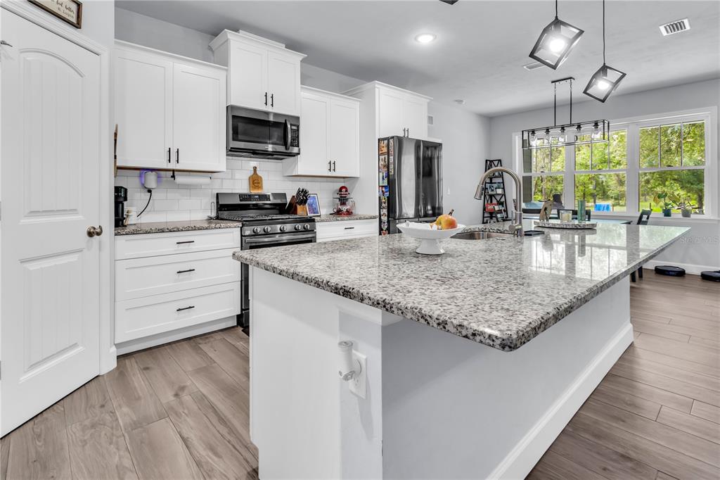 A modern kitchen features white cabinets, granite countertops, a large island, and wood-look flooring — 8069 NE 8TH PLACE, HIGH SPRINGS, FL