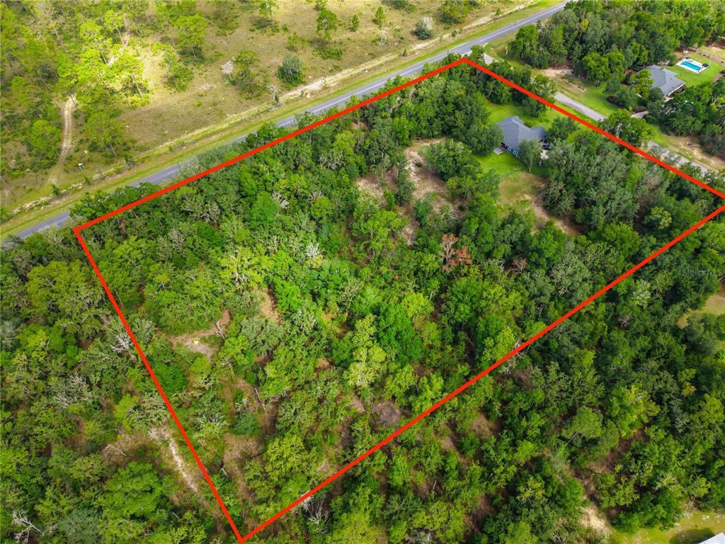 An aerial view shows a wooded lot outlined in red with a house nestled inside — 8069 NE 8TH PLACE, HIGH SPRINGS, FL