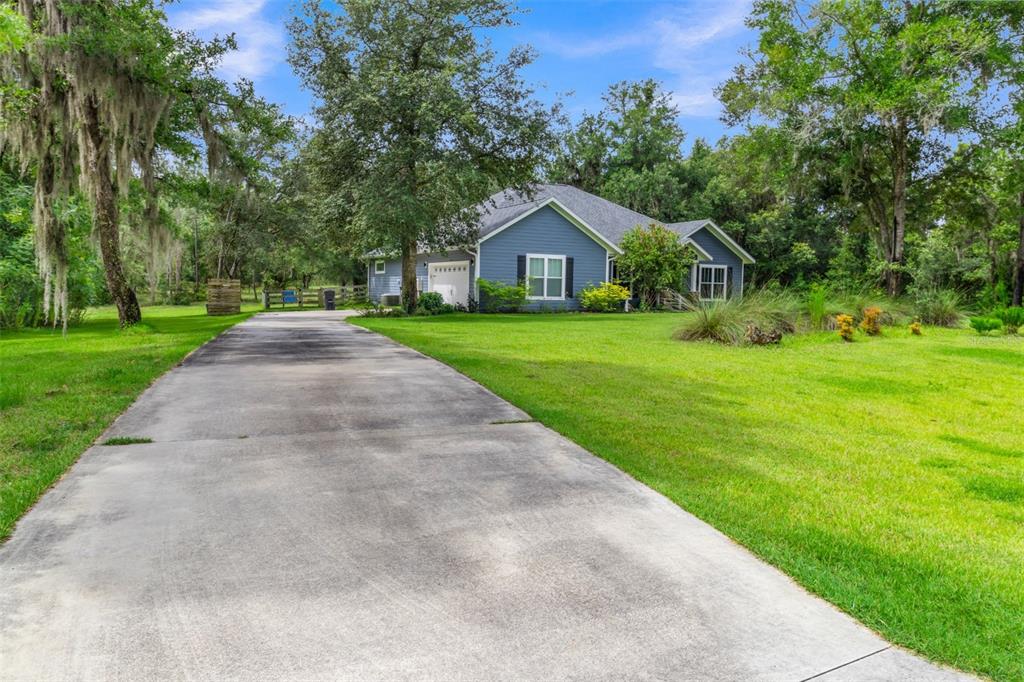 A blue house with a concrete driveway sits on a large, tree-filled grassy lot — 8069 NE 8TH PLACE, HIGH SPRINGS, FL