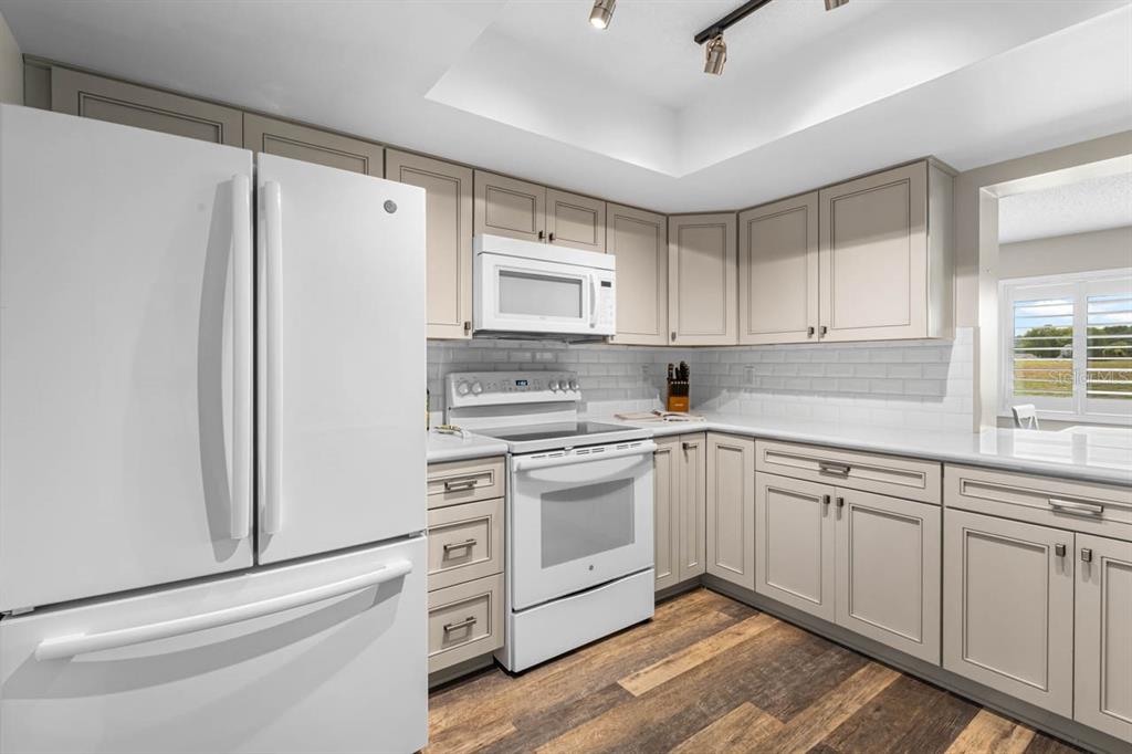 A kitchen with white appliances, light-colored cabinets, subway tile backsplash, and wood-look flooring — 1226 HADDINGTON CIRCLE, SUN CITY CENTER, FL
