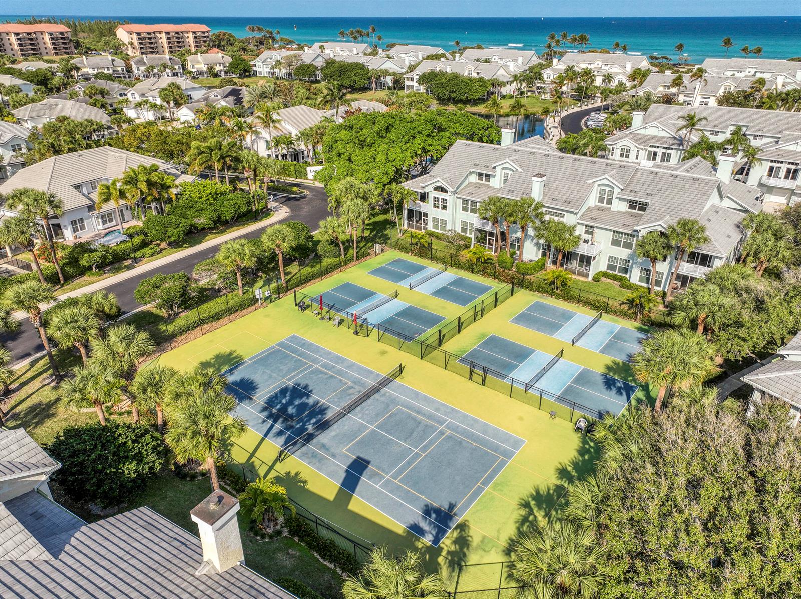 An aerial view shows tennis courts surrounded by palm trees and residential buildings near the ocean — 3004 Mainsail Circle, Jupiter FL 33477, JUPITER, FL