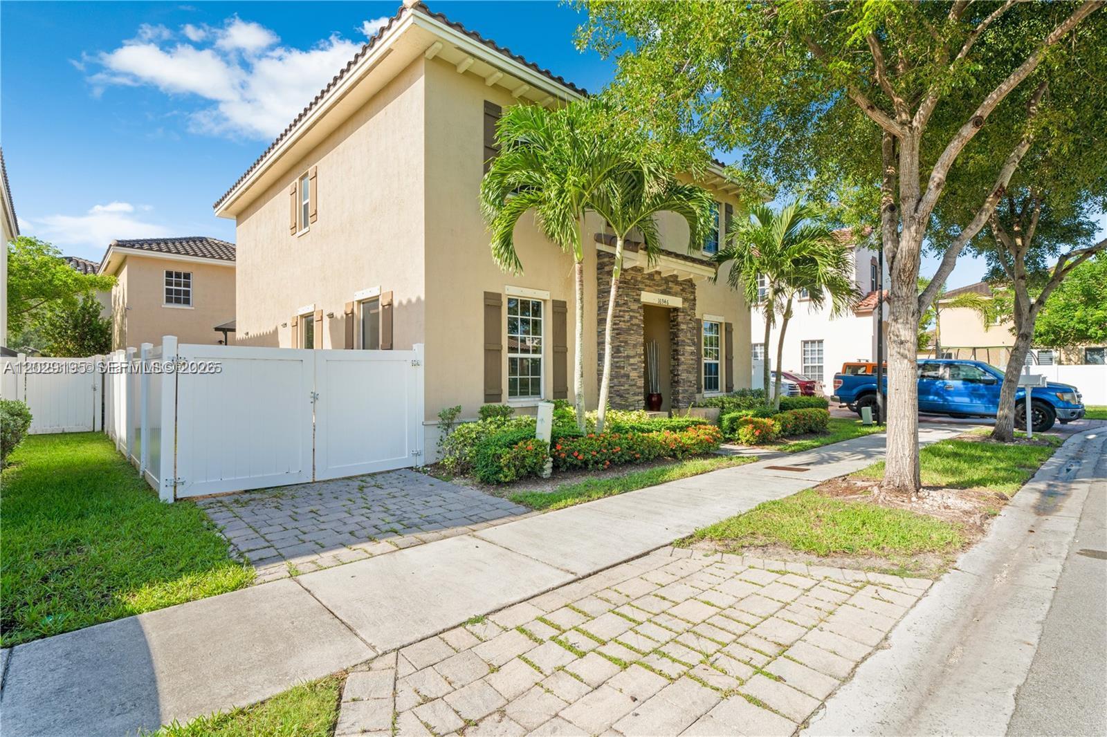A two-story tan stucco house features stone accents, brown shutters, and a white vinyl fence — 16946 SW 90th Terrace Circle, Miami FL 33196, MIAMI, FL