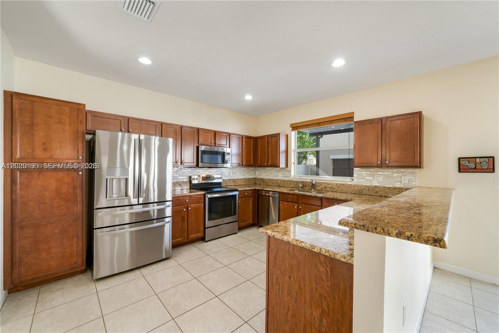 A kitchen features wood cabinets, granite countertops, stainless steel appliances, and light-colored tile flooring — 16946 SW 90th Terrace Circle, Miami FL 33196, MIAMI, FL