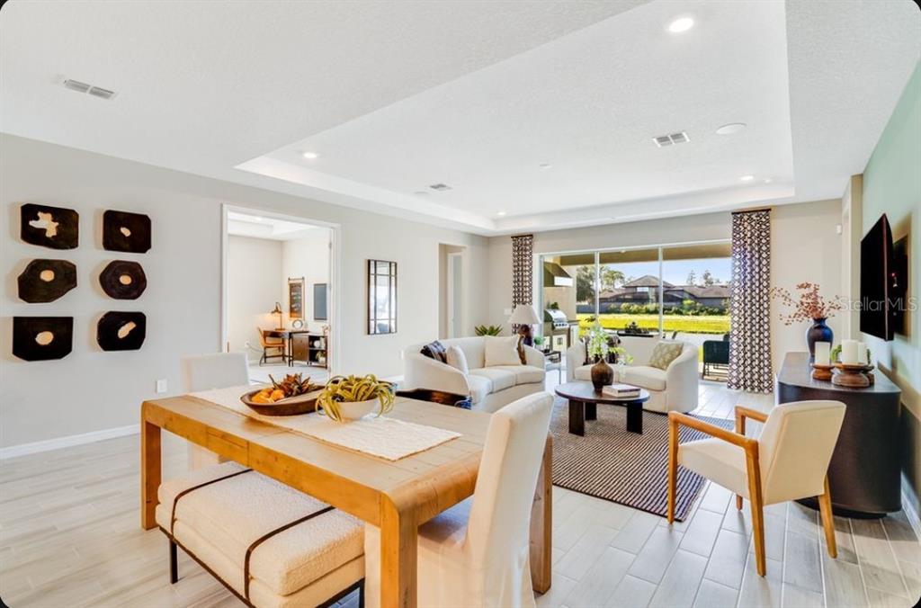 A dining area and living room with light tile floors, neutral furniture, and large sliding doors — 903 LADYFISH TRAIL, ST CLOUD, FL