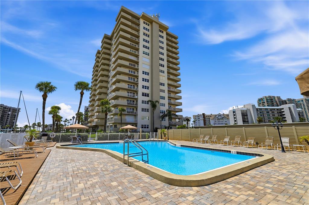 A swimming pool sits on a paved patio in front of a tall residential building — 1621 GULF BOULEVARD UNIT 1408, CLEARWATER BEACH, FL
