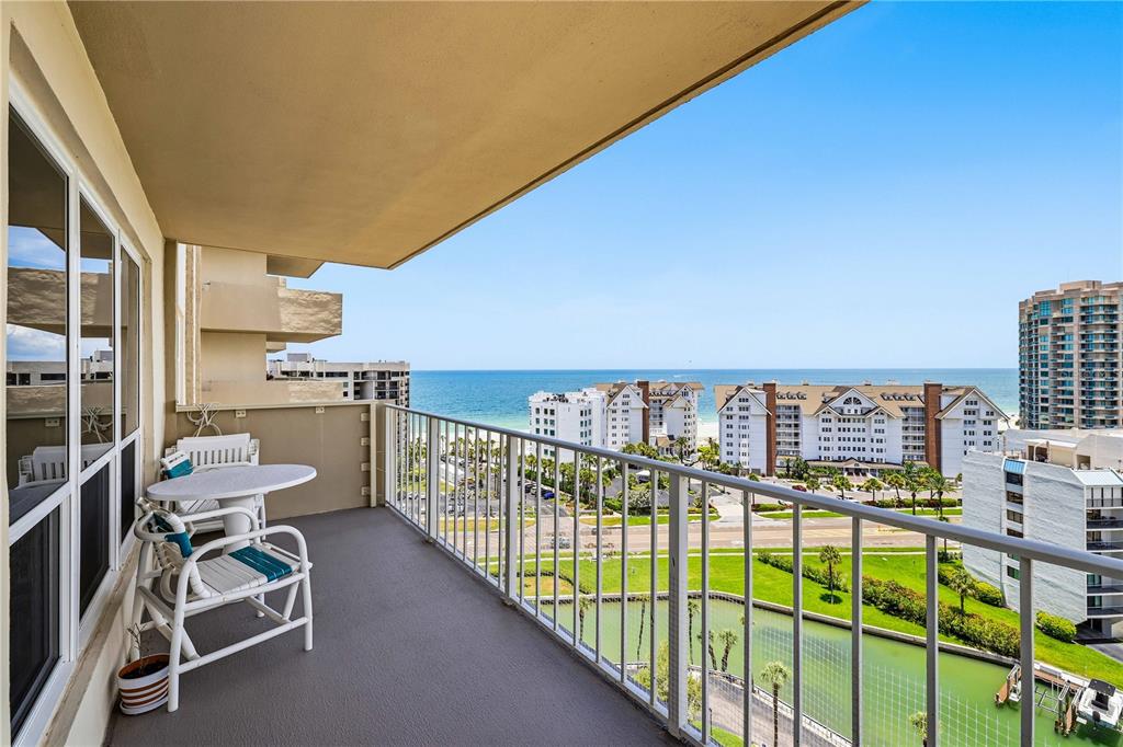 A balcony with a table and chairs overlooks a coastal view of buildings and water — 1621 GULF BOULEVARD UNIT 1408, CLEARWATER BEACH, FL