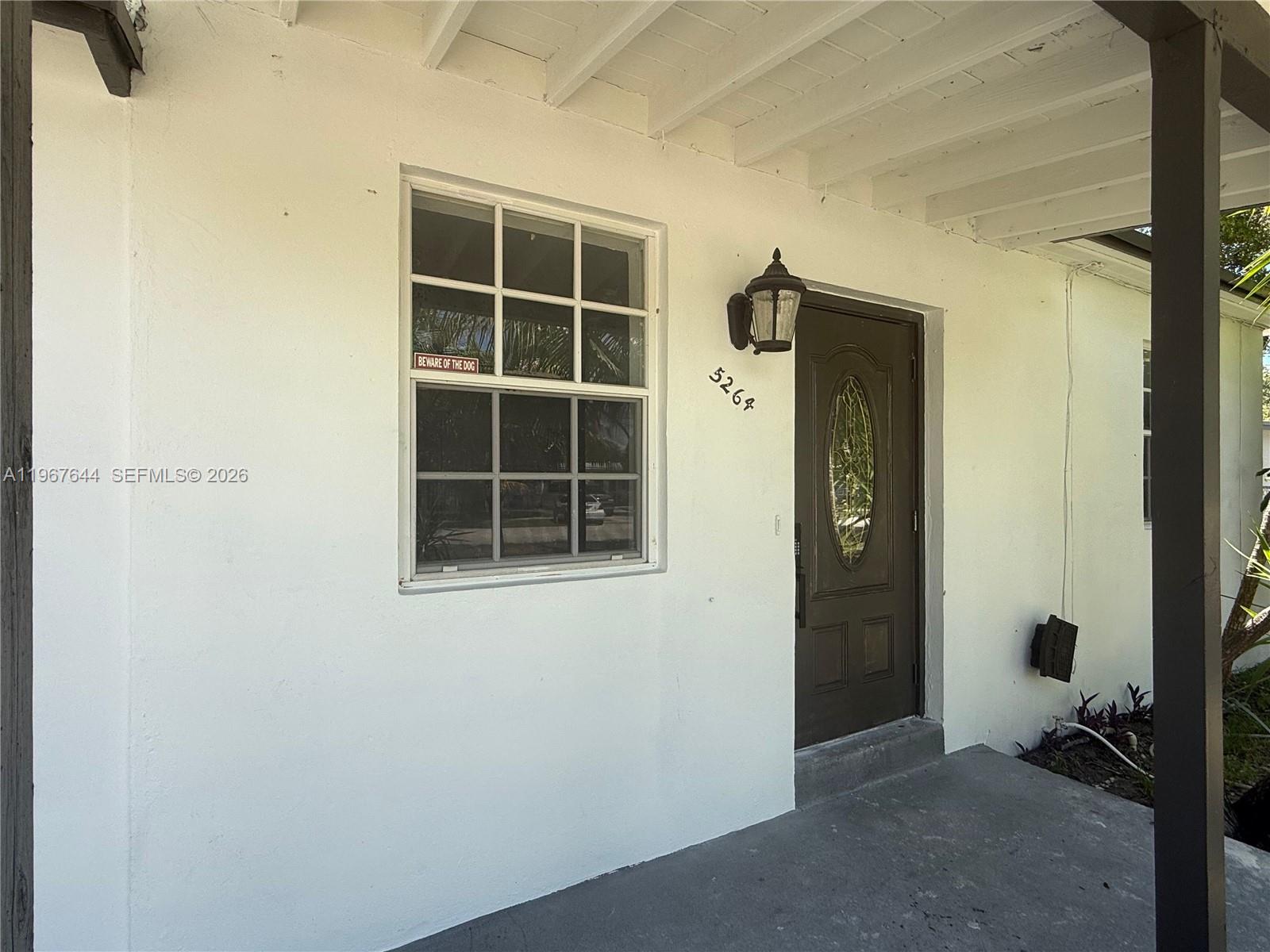 A white stucco exterior wall features a dark brown front door and a grid-paned window — 5264 NE 15th Ave, Pompano Beach FL 33064, POMPANO BEACH, FL