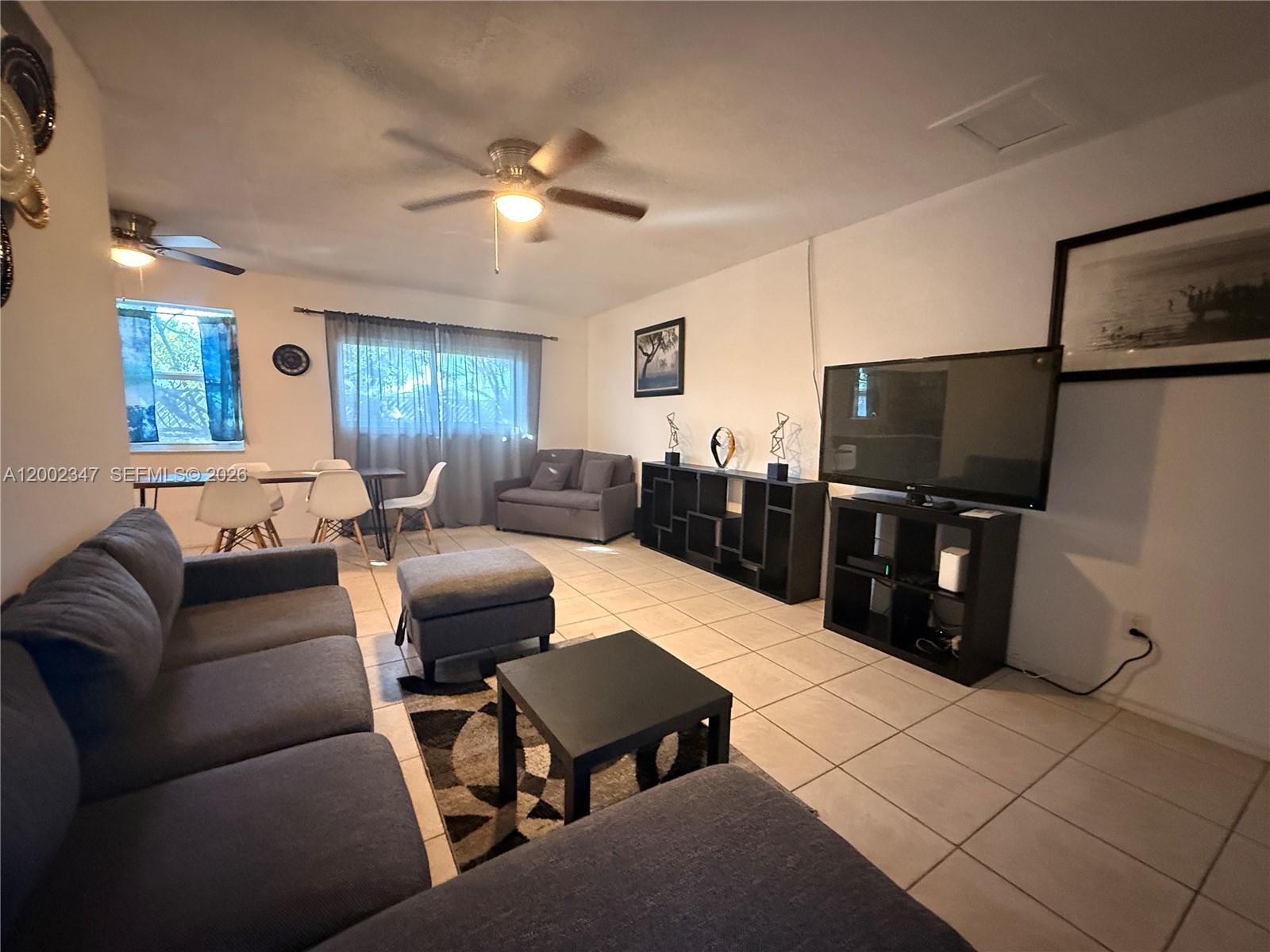 A living room features gray sofas, a television, tile flooring, and a dining area — 1104 N 17th Ct # 107, Hollywood FL 33020, HOLLYWOOD, FL