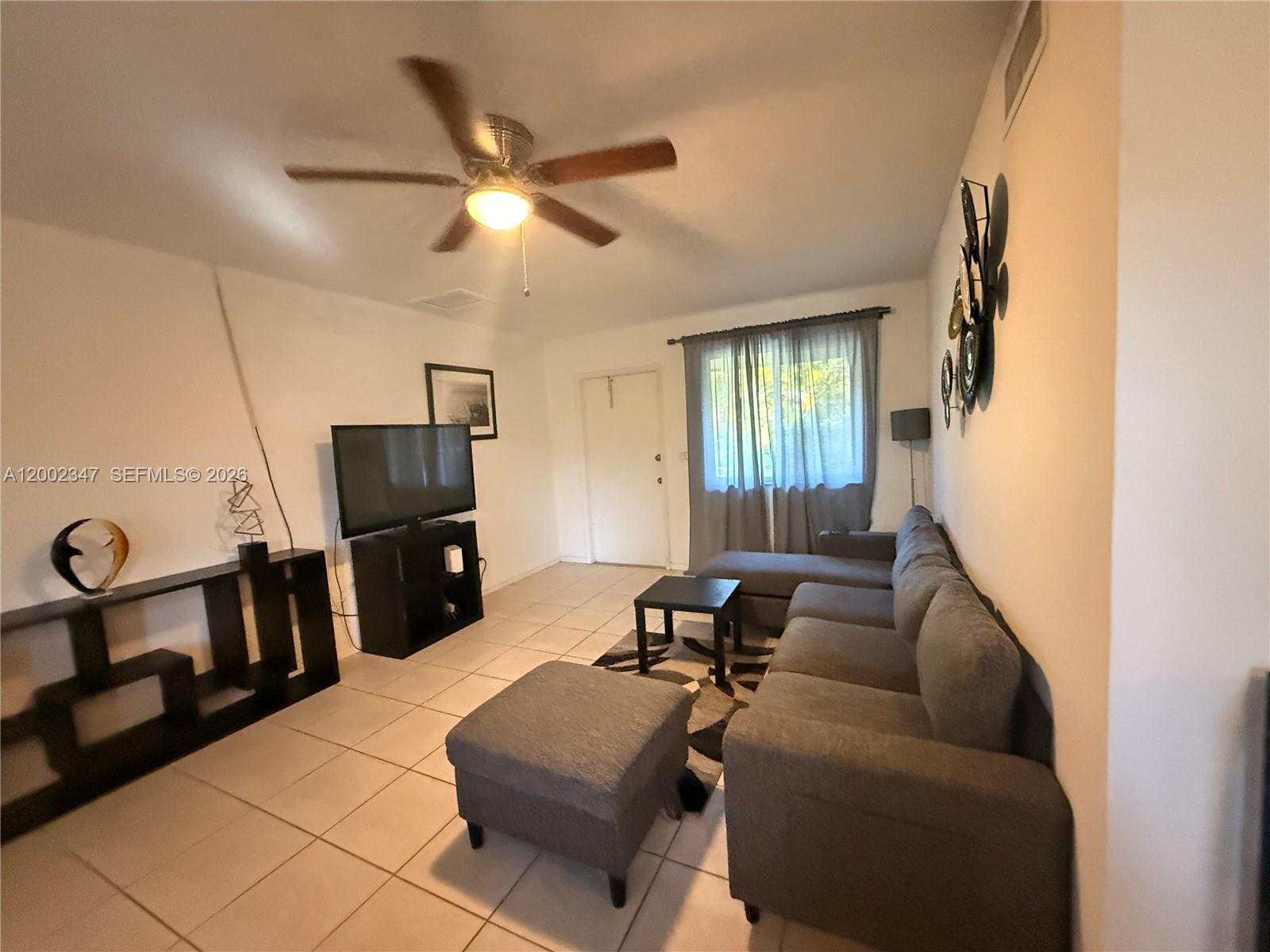 A living room features a gray sectional sofa, a television on a stand, and tile flooring — 1104 N 17th Ct # 107, Hollywood FL 33020, HOLLYWOOD, FL