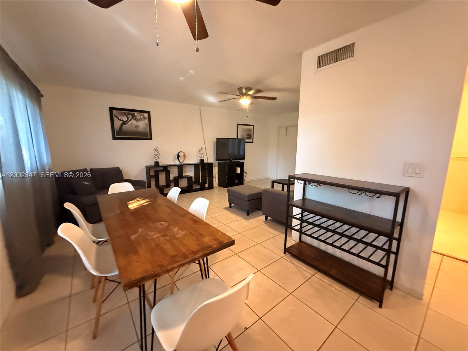 A dining area with a wooden table and white chairs opens into a living room — 1104 N 17th Ct # 107, Hollywood FL 33020, HOLLYWOOD, FL
