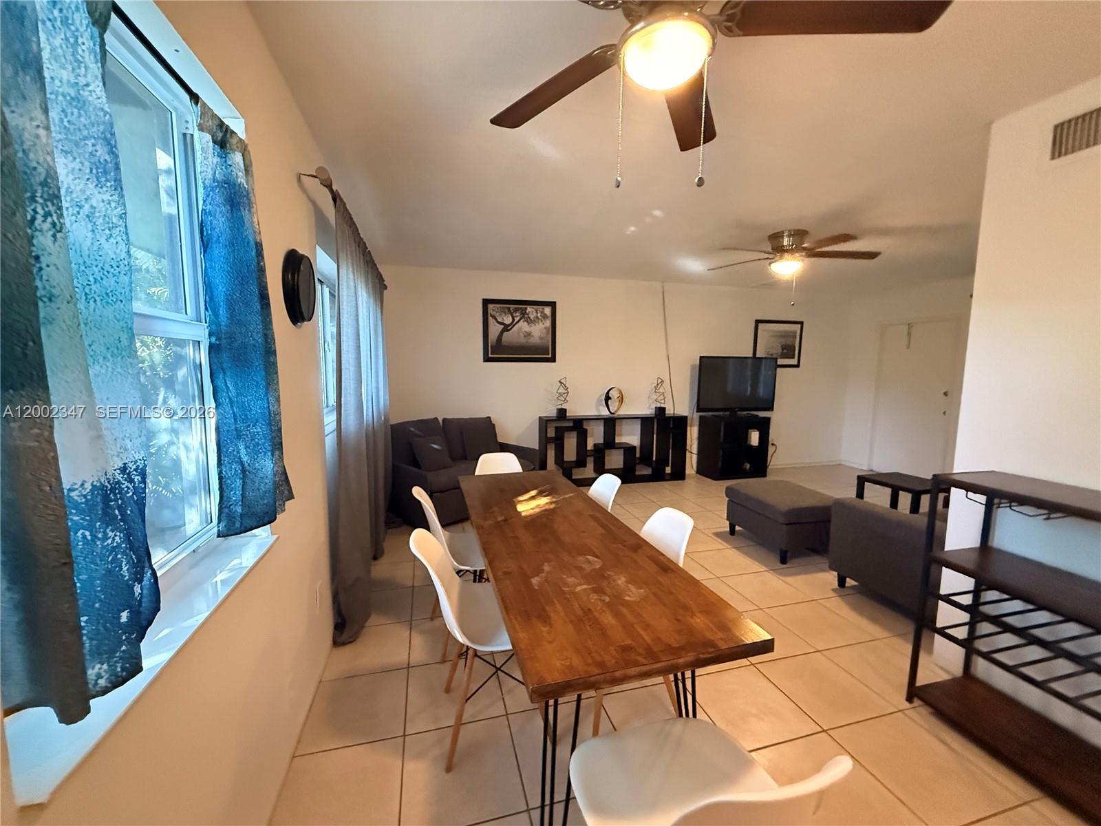 A dining area with a wooden table and white chairs opens into a living room — 1104 N 17th Ct # 107, Hollywood FL 33020, HOLLYWOOD, FL