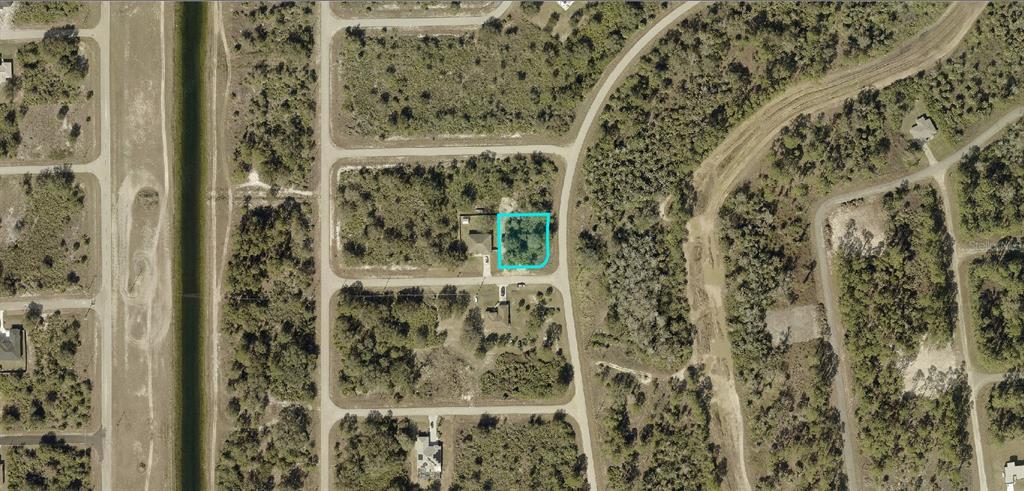 An aerial view shows a vacant, wooded residential lot outlined in blue within a neighborhood — 710 TUNNEY STREET, LEHIGH ACRES, FL