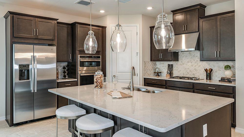 A kitchen with dark wood cabinets, stainless steel appliances, a large island, and pendant lighting — 5766 MEADS BAY POND ROAD, KISSIMMEE, FL