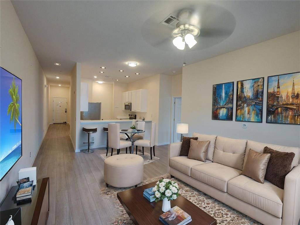 A living room and kitchen area with light wood flooring, a sofa, and dining table — 709 LUCAYA LOOP UNIT 1203, DAVENPORT, FL