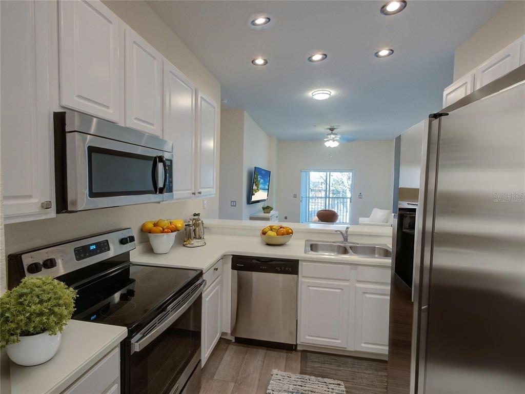 A kitchen with white cabinets, stainless steel appliances, and a view into the living area — 709 LUCAYA LOOP UNIT 1203, DAVENPORT, FL