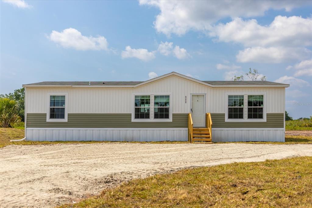 A single-story manufactured home with white and olive green siding sits on a gravel lot — 20968 NW 264TH STREET, OKEECHOBEE, FL