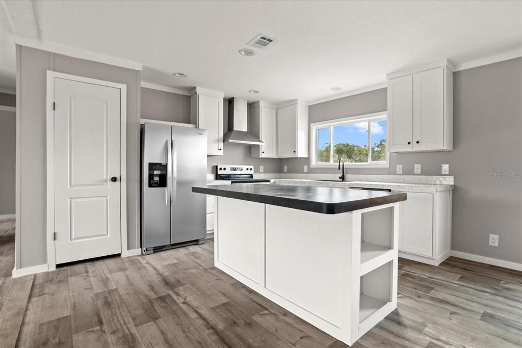 A kitchen features white cabinets, a dark island countertop, stainless steel appliances, and wood flooring — 20968 NW 264TH STREET, OKEECHOBEE, FL