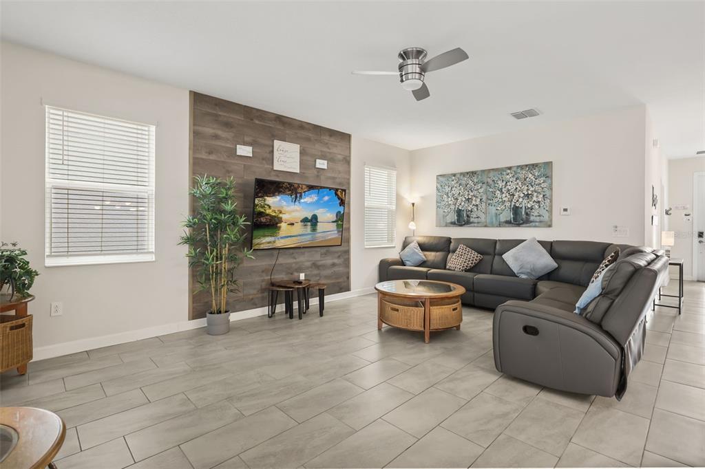 A living room features gray tile flooring, a wood-paneled accent wall, and a large sectional sofa — 740 DROP SHOT DRIVE, DAVENPORT, FL