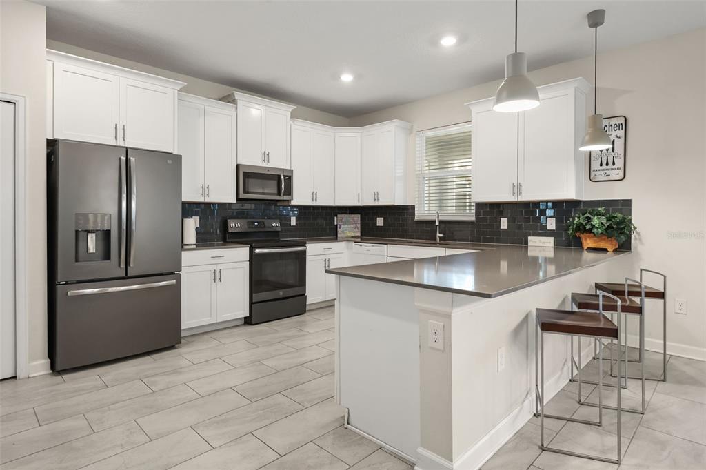 A kitchen features white cabinets, dark countertops, stainless steel appliances, and a breakfast bar — 740 DROP SHOT DRIVE, DAVENPORT, FL
