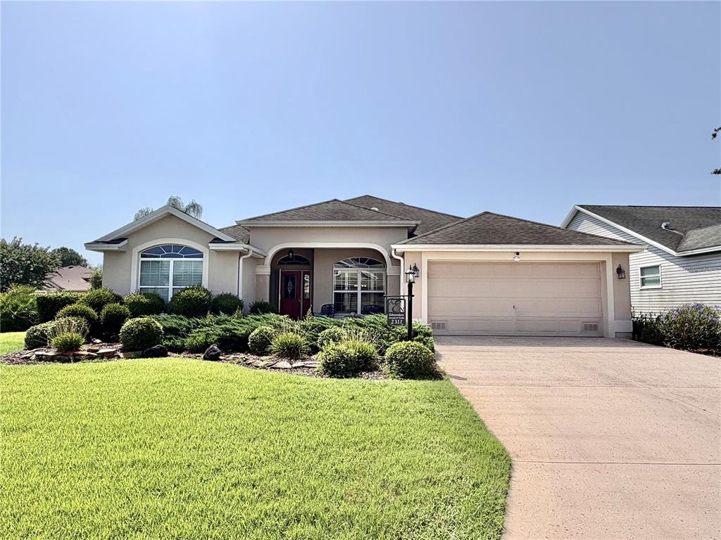 A single-story house with a beige stucco exterior, a two-car garage, and a landscaped yard — 2311 GLADE RUN, THE VILLAGES, FL