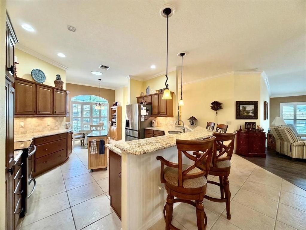 A kitchen features wood cabinets, granite countertops, a center island, and a breakfast bar — 2311 GLADE RUN, THE VILLAGES, FL