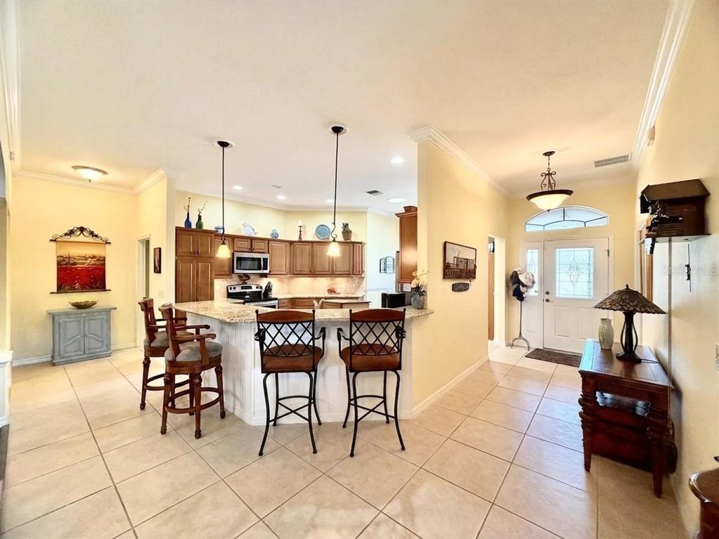 A kitchen with a granite breakfast bar, wooden cabinets, and tile flooring opens to an entryway — 2311 GLADE RUN, THE VILLAGES, FL