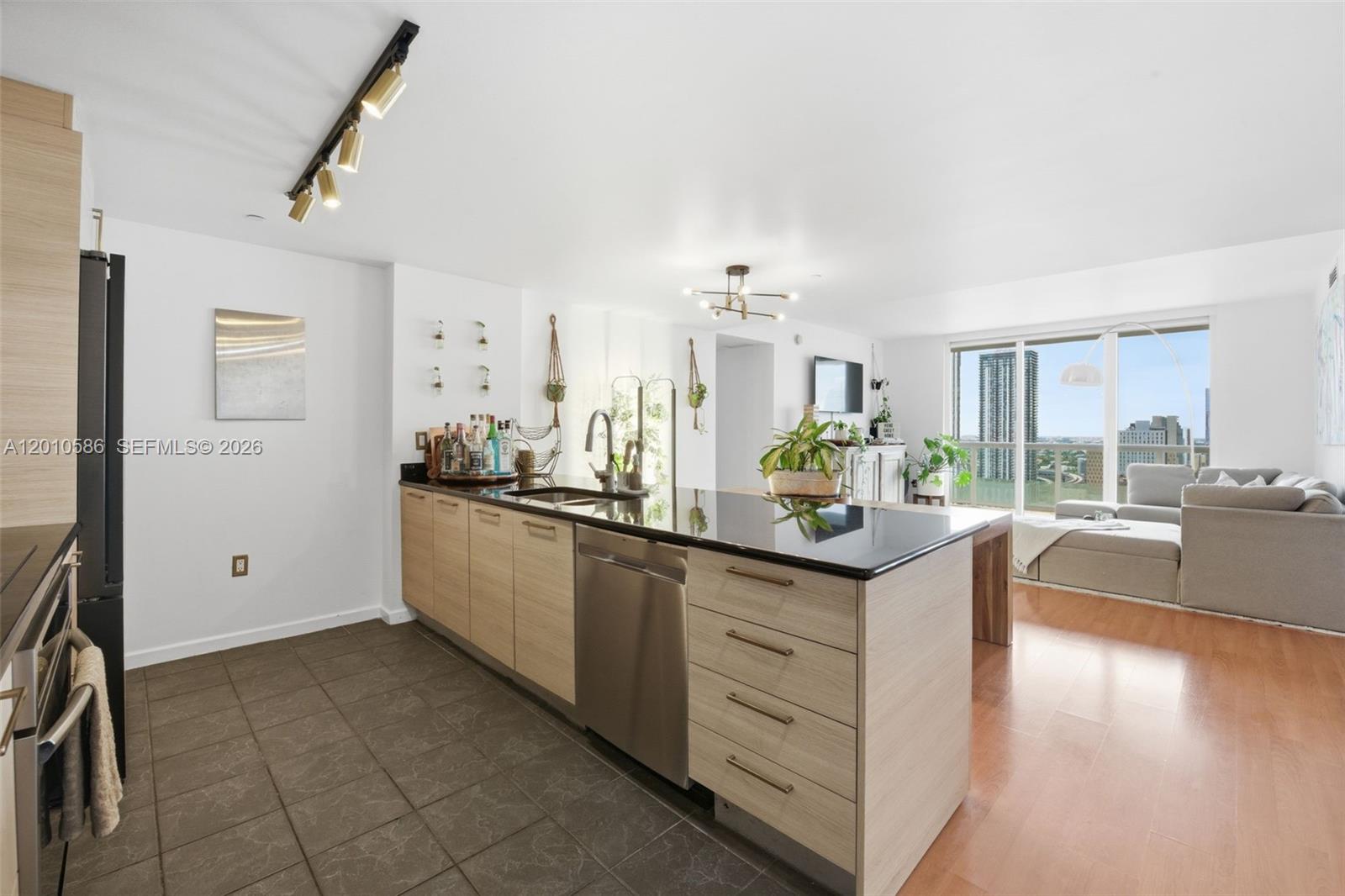 A modern kitchen with light wood cabinets and black countertops opens into a living area — 50 Biscayne Blvd # 2911, Miami FL 33132, MIAMI, FL