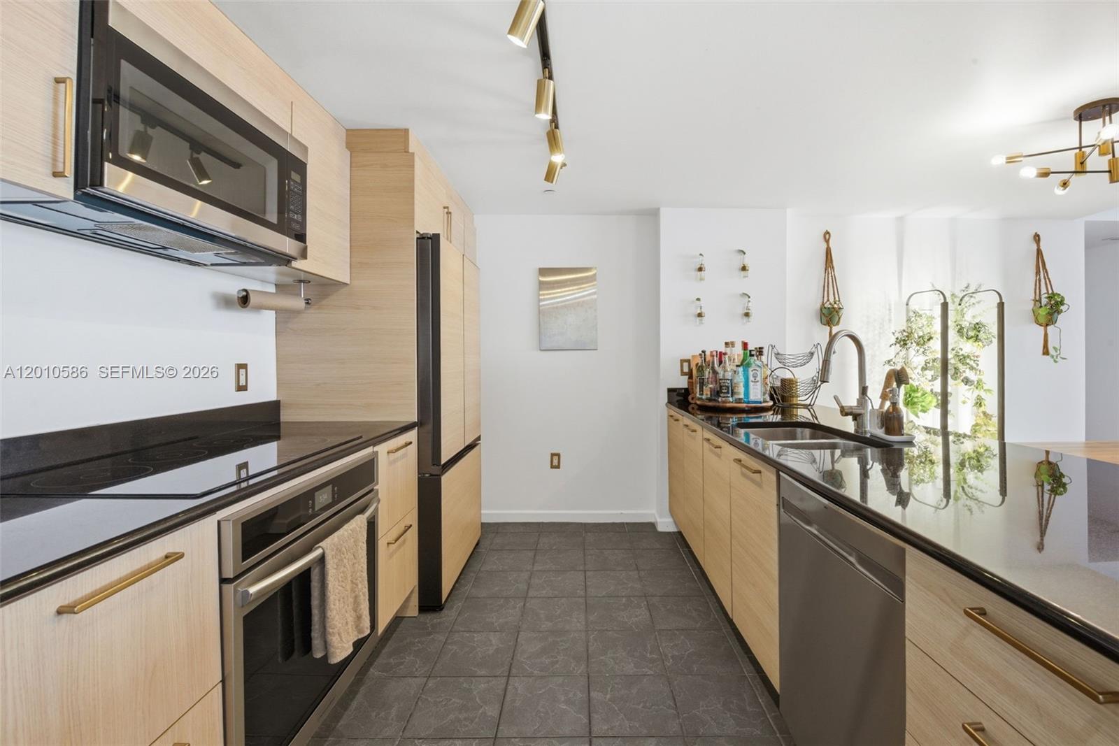 A modern kitchen features light wood cabinets, black countertops, stainless steel appliances, and tile flooring — 50 Biscayne Blvd # 2911, Miami FL 33132, MIAMI, FL