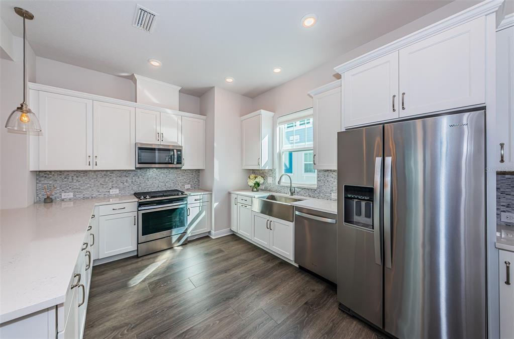 A modern kitchen features white cabinets, stainless steel appliances, a farmhouse sink, and wood flooring — 815 BURLINGTON AVENUE N, ST PETERSBURG, FL