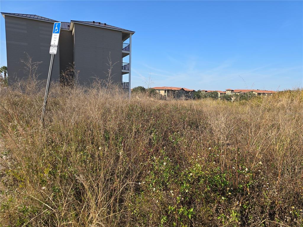 An overgrown vacant lot sits in front of a multi-story apartment building under a clear sky — 821 RETREAT BOULEVARD UNIT 102, DAVENPORT, FL