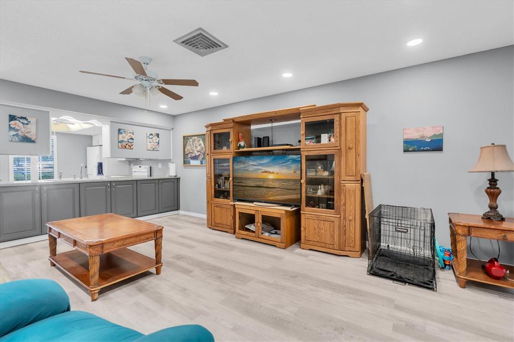 A living room features light wood-look flooring, a large wooden entertainment center, and gray cabinets — 12227 DARWOOD DRIVE UNIT B, HUDSON, FL
