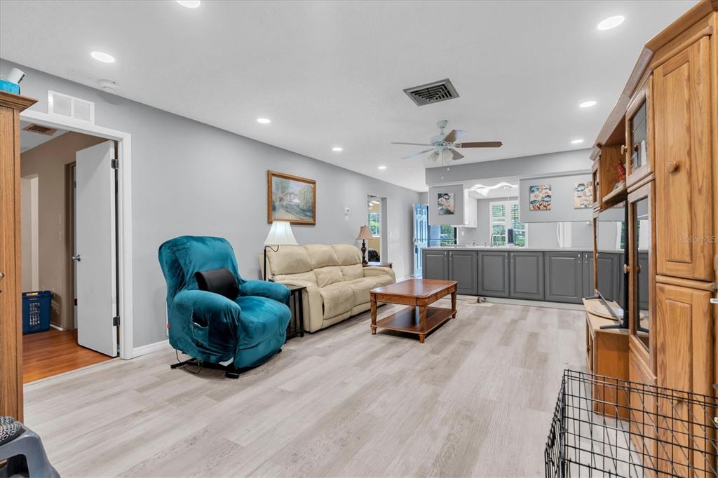 A living room features light wood-look flooring, a teal recliner, a beige sofa, and cabinetry — 12227 DARWOOD DRIVE UNIT B, HUDSON, FL