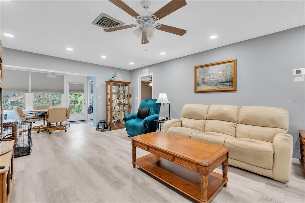 A living room features light wood-look flooring, a beige sofa, a coffee table, and a ceiling fan — 12227 DARWOOD DRIVE UNIT B, HUDSON, FL