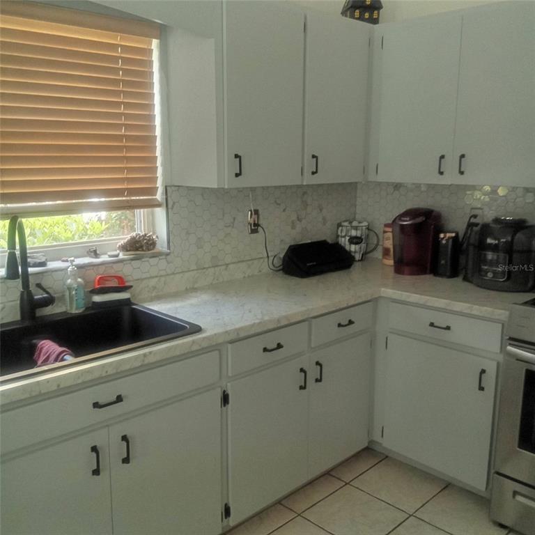 A kitchen features light-colored cabinets, a white marble-look countertop, a black sink, and tiled backsplash — 15301 MONTREAT WAY, TAMPA, FL