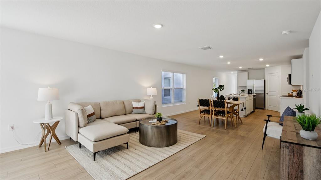 An open-concept living and dining area features light wood flooring and a beige sectional sofa — 1207 12 STREET SE, RUSKIN, FL