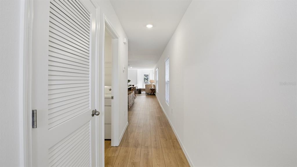 A hallway with wood-look flooring leads toward an open-concept living area and laundry closet — 1207 12 STREET SE, RUSKIN, FL